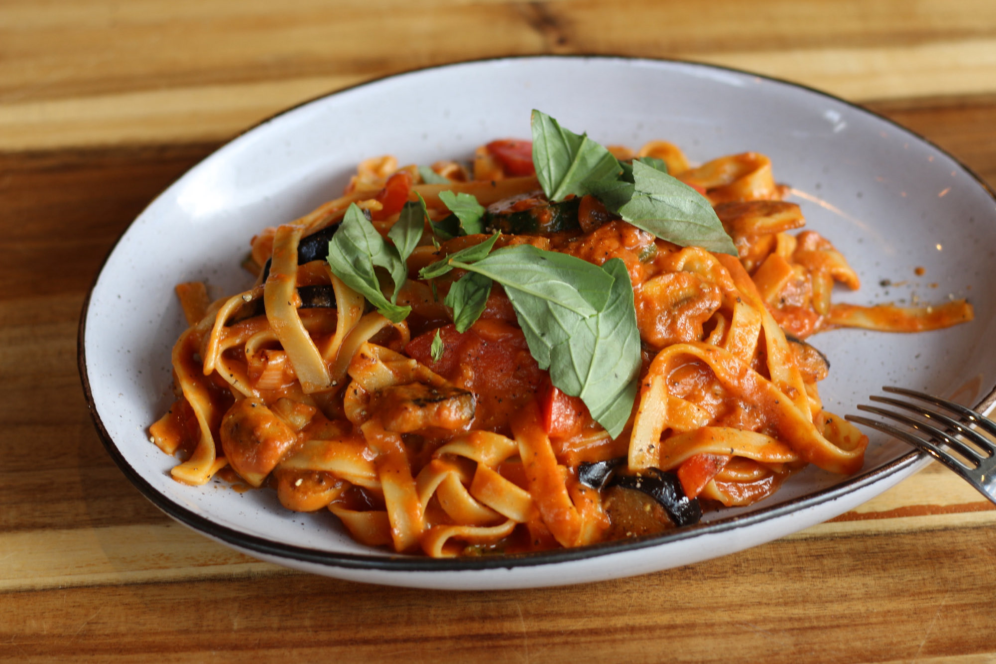 Teller Tagliatelle mit Tomatensauce und frischem Basilikum auf einem Holztisch